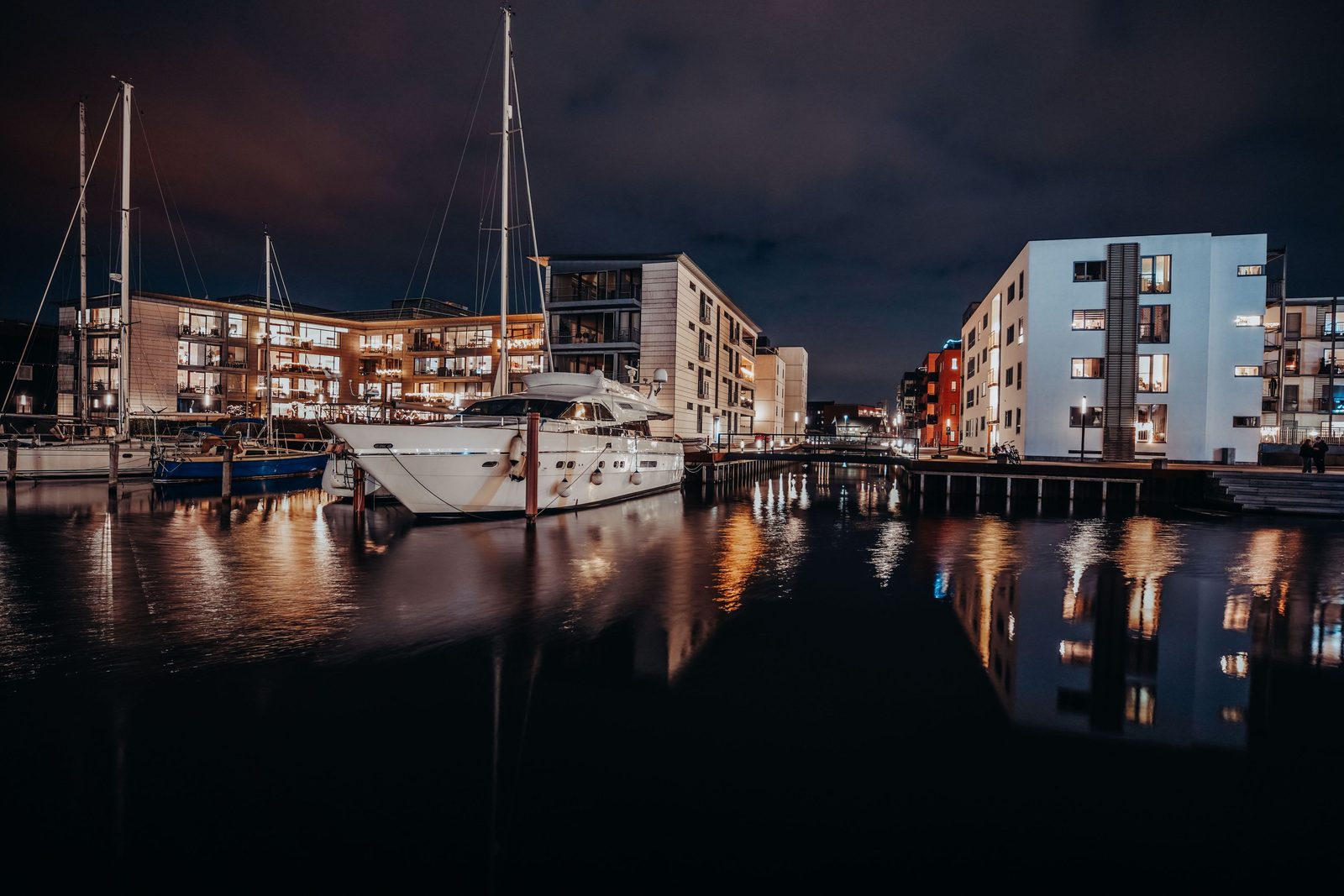 Rolig havnefront om aftenen med belyste bygninger og vand — det driftsmiljø, som meget dansk erhvervsliv arbejder fra.