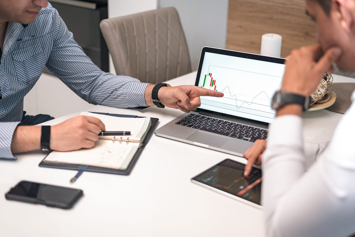 To personer analyserer finansielle data og grafer på en bærbar computer og tablet.